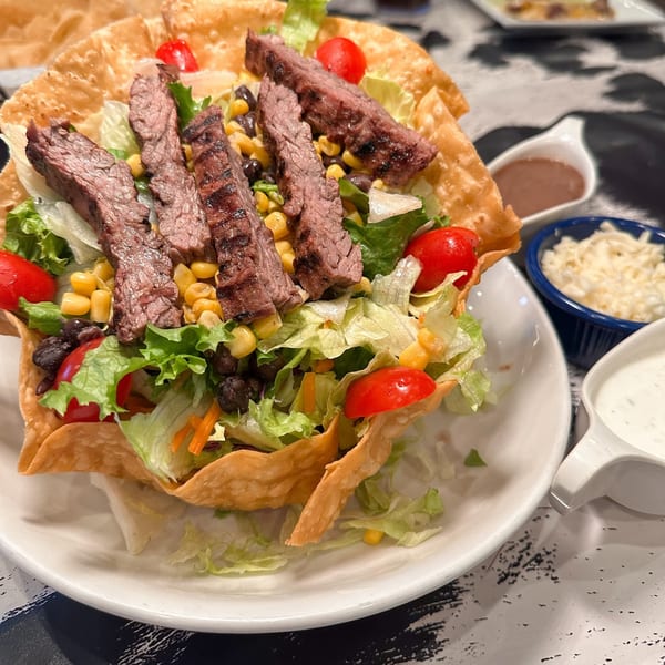 A Mariano's taco salad with grilled steak, lettuce, corn, black beans, and tomatoes in a crispy tortilla bowl.