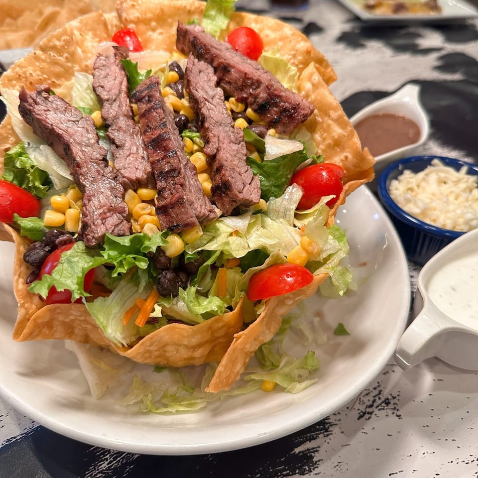 A Mariano's taco salad with grilled steak, lettuce, corn, black beans, and tomatoes in a crispy tortilla bowl.